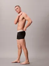 Pack de tres bóxers tipo trunk de color negro, confeccionados en algodón con elastano. Presentan una cintura elástica ancha en color blanco con el logo de la marca estampado en repetidas ocasiones.