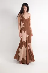 Vestido largo marrón de gasa con tirantes finos, escote en V y grandes parches decorativos en forma de flor en tonos rosados.
