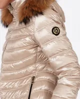 Campera puffer color beige con relleno de plumón, cierre central con cremallera de doble carro, bolsillos laterales y capucha desmontable con borde de piel sintética marrón. Largo 70cm.