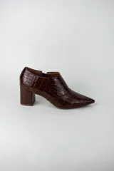 Botines de caña baja con acabado acharolado y textura efecto cocodrilo. Presentan punta fina, cierre lateral y taco cuadrado de altura media.