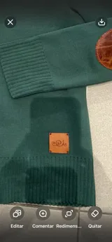 Cardigan de punto color verde oscuro, con cuello redondo, cierre frontal de botones y coderas de cuero marrón. Presenta ribetes en rib y detalle de etiqueta de cuero en el dobladillo.