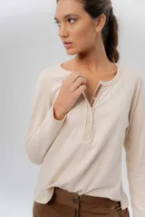 Remera manga larga color beige melange, confeccionada en algodón con spandex, con escote redondo y cartera delantera con botones y detalle de cordón tejido multicolor.