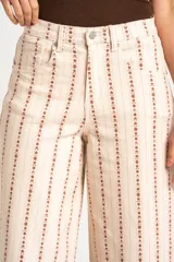 Pantalón jean wide leg de tiro alto, color beige con estampado vertical de líneas y flores marrones, de corte holgado y diseño de cinco bolsillos.