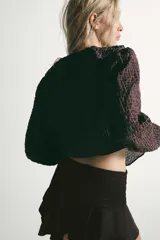Camisa de manga larga con estampado de cuadros, escote en pico con volantes decorativos y cierre frontal con botones. Presenta puños elásticos.
