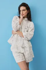 Camisa de broderie color blanco, con cuello clásico, mangas abullonadas y cierre frontal oculto.