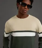 Suéter de punto con cuello redondo y manga larga, diseñado con un patrón de bloques de color en tonos beige, blanco y gris. Presenta un corte regular que se ajusta de forma anatómica al cuerpo.