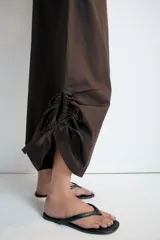 Pantalón culotte de tiro medio, color verde militar, con cintura elástica y bolsillos laterales ocultos. Presenta un diseño de bajo ancho con aberturas ajustables mediante cordones fruncidos en los laterales.