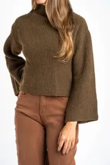Polera de lana oversize color beige melange, con cuello alto, mangas largas acampanadas y diseño de tejido acanalado con tramas direccionales.