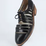 Zapato Oxford negro con cordones, capellada de cuero con textura croco y cortes calados. Taco bajo foliado y suela de goma antideslizante.
