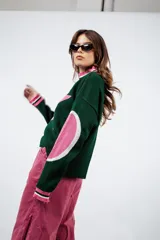 Sweater de punto color verde oscuro con cuello alto y diseño de estrella blanca con borde rosa en el frente. Tiene parches rosas en los codos y ribetes rosas y blancos en cuello, puños y ruedo.