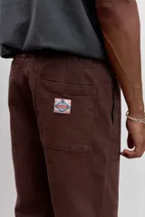 Pantalon de corte recto en color marron, confeccionado en tela resistente, con bolsillos laterales tipo parche y cierre frontal.