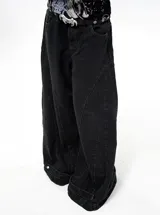 Jean de corte wide leg en color negro, con diseño de paneles verticales y ajuste en el ruedo mediante botones metálicos. Presenta tiro bajo y estructura holgada.