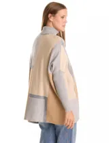 Polera tipo poncho de corte oversize, con cuello alto tejido y mangas largas con puños elásticos. Presenta un diseño geométrico de bloques de color en tonos beige, gris y tostado.