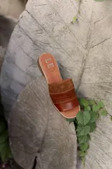 Sandalias tipo chinela de cuero, con diseño de banda ancha que combina cuero liso, cuero texturizado y gamuza en tonos marrones. Presenta plantilla con logo grabado.