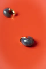 Aros tipo argolla pequeña con diseño semicircular, combinando una pieza de resina jaspeada en tonos azul oscuro con un detalle metálico dorado brillante.