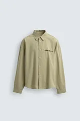 Camisa de corte boxy fit confeccionada en tejido de algodón con estampado de cuadros. Presenta cuello solapa, manga larga con puños abotonados, bolsillo plastrón en el pecho y cierre frontal de botones. Incluye un bordado a contraste en el pecho.