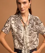 Blusa de chiffon con estampado de serpiente en tonos beige y marrón. Tiene cuello alto con lazo y mangas cortas.