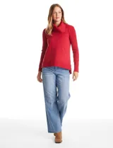 Buzo de punto color beige con cuello volcado amplio, mangas largas acanaladas y torso liso. Presenta una costura central vertical, ruedo con tajos laterales y largo asimétrico, siendo más largo en la parte posterior.
