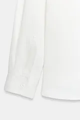 Camisa de cuello solapa y manga larga, confeccionada en tejido satinado de acabado fluido. Presenta cierre frontal con botones y bajo asimétrico.