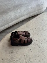 Sandalias de cuero marrón con tiras entretejidas y suela de goma negra.