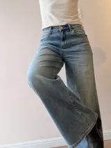 Pantalón de jean con corte wide leg y tiro medio-alto. Presenta un lavado gris azulado desgastado con acabado vintage y ruedo desflecado.