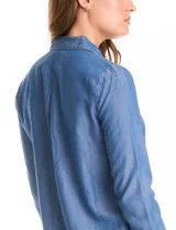Blusa de lyocell color azul con efecto denim, cuello camisero con solapa y escote en V con cierre de un botón. Presenta mangas largas con terminación doblada y ruedo redondeado.