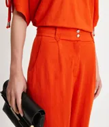 Pantalón zanahoria color naranja, marca Cortelle, con pliegues, bolsillos laterales y traseros, detalle de botón en los bajos y cierre en la cintura por botón.