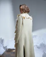 Tapado largo color natural de lana merino afieltrada, con cuello grande formado por piezas horizontales. Tiene bolsillos laterales y se puede usar suelto o cerrado con un accesorio.