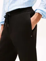 Pantalón de jogging negro de corte regular y pierna cónica, confeccionado en mezcla de algodón y poliéster. Presenta cintura con cordón, bolsillos laterales y trasero, y logo de Tommy Hilfiger bordado en la cadera.