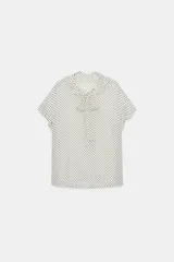 Blusa de viscosa con estampado de lunares, cuello redondo con escote en pico, volantes y lazada frontal. Presenta manga corta y bajo recto.