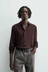 Camisa de manga larga color marrón oscuro, con cuello solapa y cierre frontal de botonadura. El tejido es semitransparente y presenta una textura jacquard.