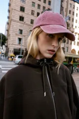 Chaqueta estilo bomber de corte oversize en color marrón oscuro, confeccionada en tejido suave. Presenta capucha con cordones ajustables, cierre frontal con cremallera, mangas largas con puños elásticos y bolsillos delanteros de vivo. El bajo cuenta con detalle de pliegues.