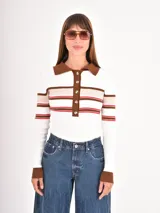 Buzo de tejido de punto con cuello polo y cierre frontal de botones. Presenta un diseño a rayas horizontales en tonos blanco, marrón y rojo, con mangas largas y puños en contraste.