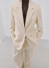Blazer de diseño recto y estilo sastrero, color beige, confeccionado en mezcla de lyocell y poliéster. Cuenta con cuello en pico con solapas de muesca, manga larga, bolsillos delanteros con solapa y cierre frontal de un botón.