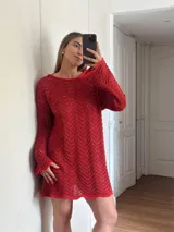 Vestido corto de tejido calado con patrón de ondas, confeccionado en algodón y lurex. Presenta mangas largas, cuello redondo y diseño holgado.