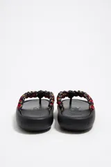 Sandalia de dedo con base plana color negro y tira de tela trenzada multicolor.