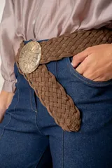 Cinturón trenzado de cuero sintético efecto gamuza, con hebilla circular metálica grande y ornamentada.