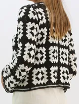 Cardigan abierto de tejido de punto calado con diseño geométrico y floral bicolor. Presenta escote en V, mangas largas y cierre frontal con tiras para anudar. Incluye detalles de vivos a contraste en el contorno del escote, puños y ruedo.