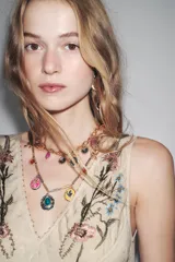 Pack de tres collares superpuestos con cadenas mixtas en tonos dorado y plateado. Incluyen múltiples dijes colgantes con piedras de colores (turquesa, rosa, ámbar, violeta) y motivos florales y de insectos.