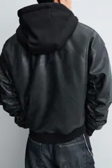 Cazadora estilo bomber de corte relajado confeccionada en tejido efecto piel color negro. Presenta capucha integrada, cierre frontal de cremallera, bolsillos laterales de vivo y puños y bajo con acabado en rib. El interior cuenta con forro acolchado en color naranja.