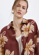 Camisa de manga larga color marrón con estampado floral grande en tonos beige y blanco, cuello camisero y cierre frontal con botones.