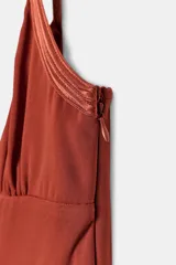 Vestido largo de corte recto y color teja, con escote en V y tirantes finos. Presenta detalles de acabados en tejido satinado combinado a tono en el escote y cierre lateral con cremallera oculta.