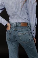 Camisa de algodón a rayas verticales celestes y blancas con terminaciones en contraste con pespuntes y ojales en color azul acero.