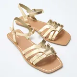 Sandalias planas color dorado, con múltiples tiras delanteras cruzadas y tira ajustable al tobillo con hebilla metálica.