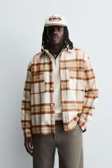 Camisa de corte relajado confeccionada en tejido con acabado de franela. Presenta diseño de cuadros en tonos beige, marrón y amarillo, cuello solapa, manga larga con puños abotonados, bolsillos plastrón en el pecho y cierre frontal de botones.