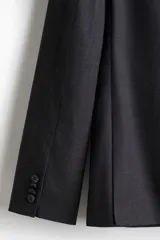 Blazer gris oscuro de corte slim fit, con solapas de muesca finas, ojal decorativo, botonadura sencilla, bolsillo superior insertado, bolsillos delanteros con solapa, dos bolsillos interiores, botones decorativos en los puños y abertura doble atrás.