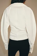 Top de tejido combinado color blanco, con cuello solapa, escote en V y cierre frontal con botones. Presenta mangas largas con puños anchos.