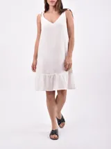 Vestido corto color rojo, de corte recto y holgado, con escote en V y tirantes anchos formados por lazos para atar en los hombros. Cuenta con un volante sutil en el ruedo.