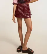 Short pollera de tiro medio confeccionado en poliuretano con acabado símil cuero. Presenta diseño de corte recto, cierre frontal con cremallera, trabillas para cinturón y dos bolsillos delanteros con solapa.