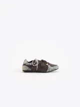 Zapatillas de cuero vacuno en color beige, con recortes de gamuza en la puntera y talón, doble cordón en tonos gris y marrón, hebilla lateral y dije colgante en la cordonera. Suela plana de goma.